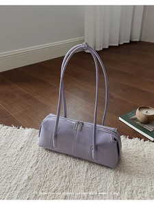 Dettaglio borsa cilindrica lilla con manici lunghi appoggiata su un tappeto bianco