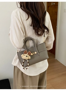 Detail of grey pebble leather handbag with gold twist lock and a cute bear charm
