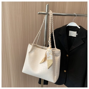 Detail of beige quilted tote bag with woven straps and geometric silk scarf accessory