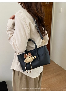 Detailed view of black pebbled leather tote bag with cute bear charm worn by a model