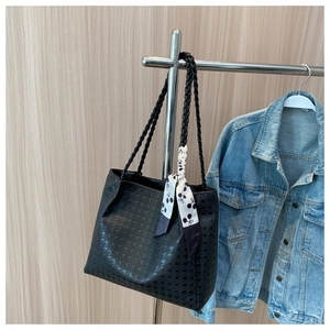 Detail of black embossed tote bag with woven handles and decorative scarf on a hanger