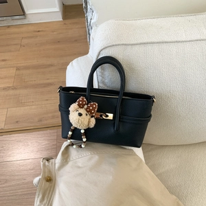Close-up of black litchi grain leather tote with gold twist lock and plush bear charm