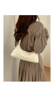 Detail of a creamy white crescent bag with pebble texture styled with pleated clothing