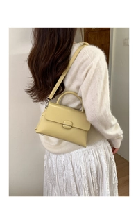 Detail showing the creamy yellow square bag worn on the shoulder with white outfit