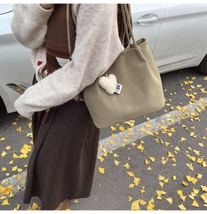 Close-up of khaki tote bag with plush heart charm on model in autumn park setting