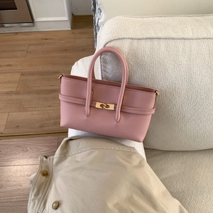Detail of pink lychee grain leather tote bag with gold lock on a fabric sofa