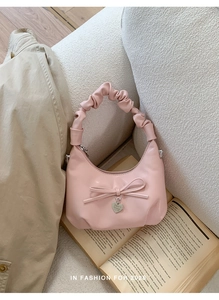 Detail of pink hobo bag featuring a pleated handle, bow decoration, and silver heart pendant