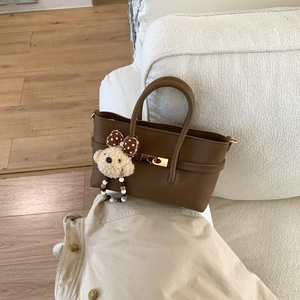 Detail of dark brown pebble leather tote bag featuring a gold clasp and cute bear charm