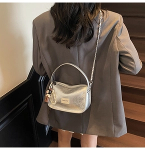 Détail du sac argenté métallisé avec bandoulière chaîne et breloques sur blazer gris