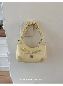 Detail of a light yellow PU leather bucket bag with bow tie and heart-shaped metal pendant