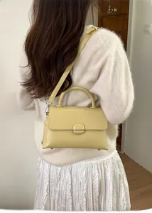 Modern light yellow square handbag with glossy finish and round handle worn as crossbody bag