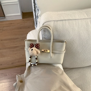 Detail of off-white lychee texture tote bag with gold twist lock and cute bear charm