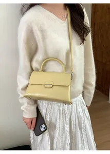 Detail showing the light yellow patent leather texture and elegant clasp of the handbag