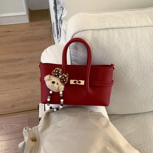Detail of red pebbled leather handbag with golden lock and cute plush bear charm