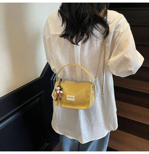 Détail d'un sac à main jaune en cuir verni avec bandoulière et pendentif poupée