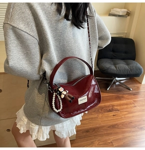 Détail du sac à main bordeaux avec breloque perle et plaque de marque en métal