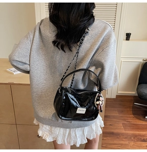 Détail du sac bandoulière plissé noir brillant avec chaîne et breloque en perle