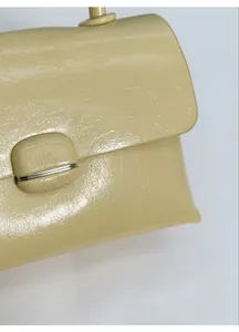 Close-up of beige leather handbag featuring a glossy finish and round metallic buckle
