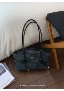 Détail du sac cabas en denim gris foncé avec logo doré et lanières en cuir à nœuds élégants