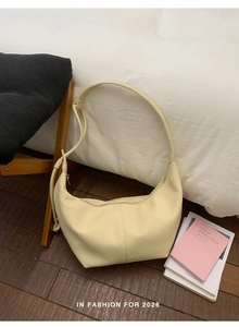 Detail of minimalist beige croissant hobo bag with litchi grain texture on white bedding