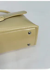 Close-up of the wide base of a beige leather handbag showing silver metal studs and stitching