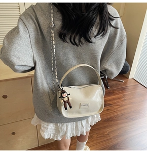 Détail d'un sac bandoulière en cuir verni crème avec bandoulière chaîne et pendentif poupée