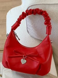 Chic red crescent handbag with ruched handle, bow detail, and heart pendant on sofa