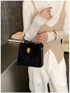 Detail of minimalist black bucket bag with a golden square twist lock and smooth texture