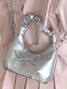 Silver metallic bucket bag with bow detail and chain strap worn over pink coat