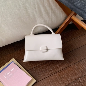 Detailed close-up of a white square handbag with a glossy finish and top handle on wooden floor