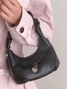 Fashionable black crescent shoulder bag with bow and heart pendant on pink coat background