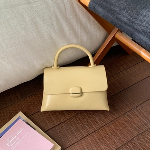 Detail shot of a cream-yellow leather handbag with smooth texture on a dark wood floor