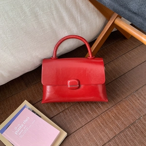 Detail of a red glossy leather handbag with a vintage metal buckle and a sturdy handle