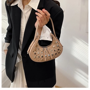 Close-up of beige half-moon bag with silver metal rivets worn by a model in a black blazer