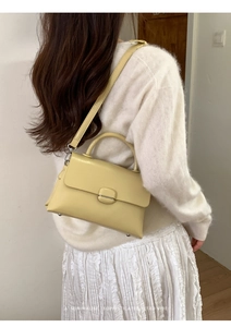 Detailed side view of minimalist light yellow leather handbag worn by a model