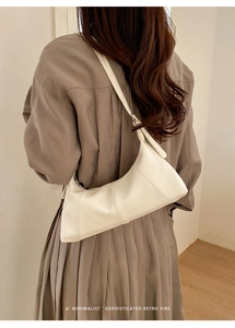 Minimalist beige leather shoulder bag worn over the shoulder against a soft retro backdrop