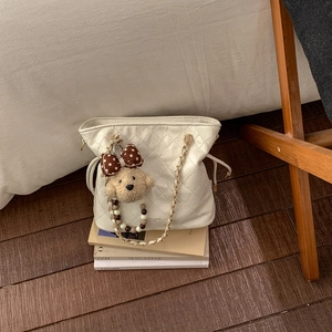 Close-up of beige quilted bucket bag with teddy bear charm and gold chain strap