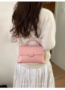 Back view of model wearing a glossy light pink square handbag with adjustable shoulder strap
