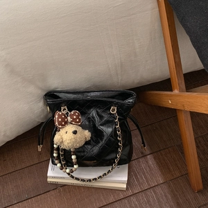 Detail of black quilted bucket bag with chain strap and cute bear charm pendant