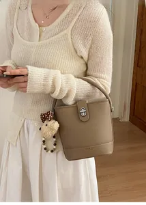 Detail of khaki leather bucket bag with silver twist lock and plush bear charm accent
