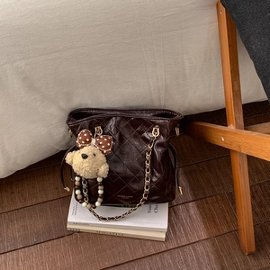 Detail of coffee brown quilted bucket bag with gold chain strap and bear charm