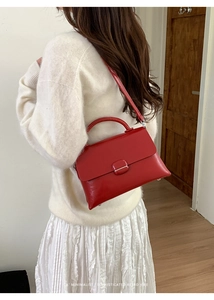 Detail view of red glossy patent leather handbag with metal buckle and shoulder strap