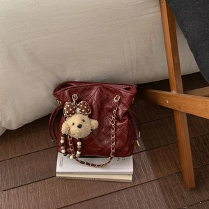 Close-up of burgundy quilted bucket bag with gold chain strap and plush bear charm