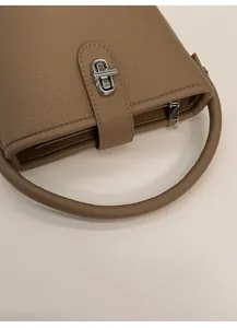 Detail view of khaki lychee grain leather handbag featuring metal twist lock and handle