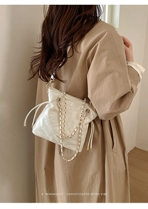 Detailed view of white quilted bucket bag with gold chain strap on model's shoulder