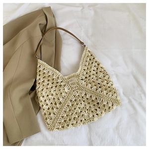 Detail of hollow mesh woven straw tote bag with brown leather shoulder strap and metal ring