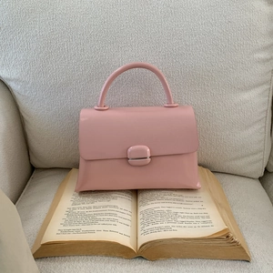 Pink minimalist leather handbag with round buckle placed on a vintage book in a soft setting