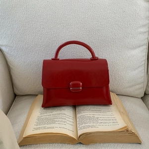 Close-up of red glossy leather handbag placed on a vintage book for detail view