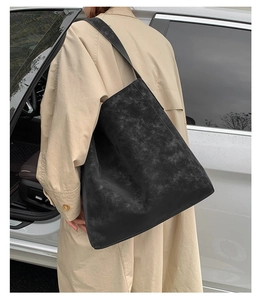 Scatto esterno di una borsa tote nera opaca con tracolla larga su un trench coat