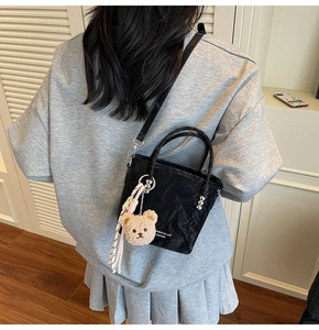 Détail d'un sac seau noir plissé avec breloque ours en peluche et foulard rayé décoratif